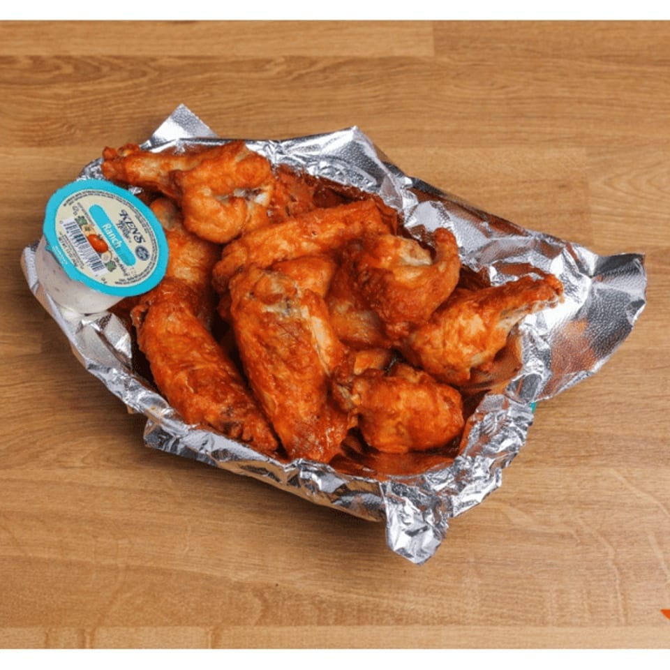 Crispy buffalo chicken wings served in a foil-lined basket with blue cheese dipping sauce on a wooden table.