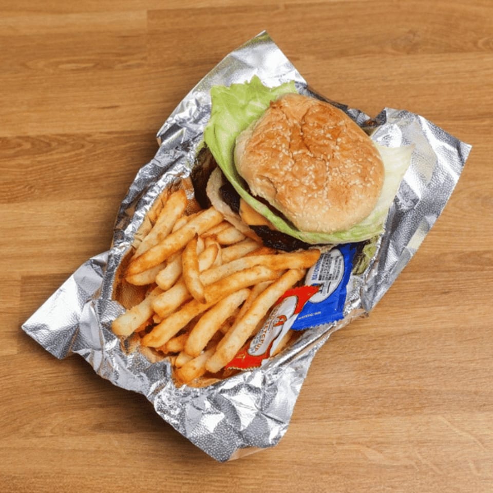 Sesame-seed hamburger with lettuce, fries, and condiment packets served in foil on a wooden table.