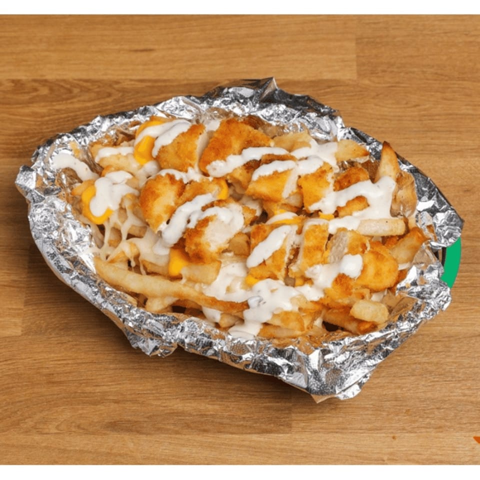 Loaded foil tray of crispy chicken pieces and fries topped with melted cheese and white sauce on a wooden table.